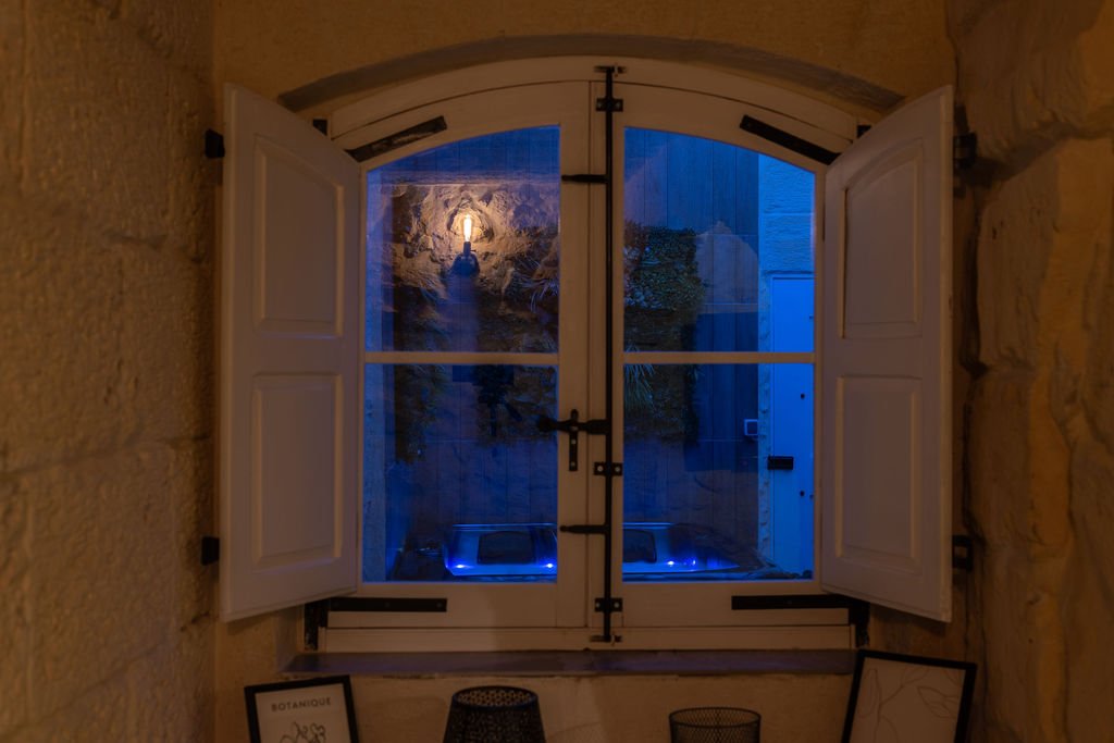 Evening view of the illuminated hot tub through a traditional window